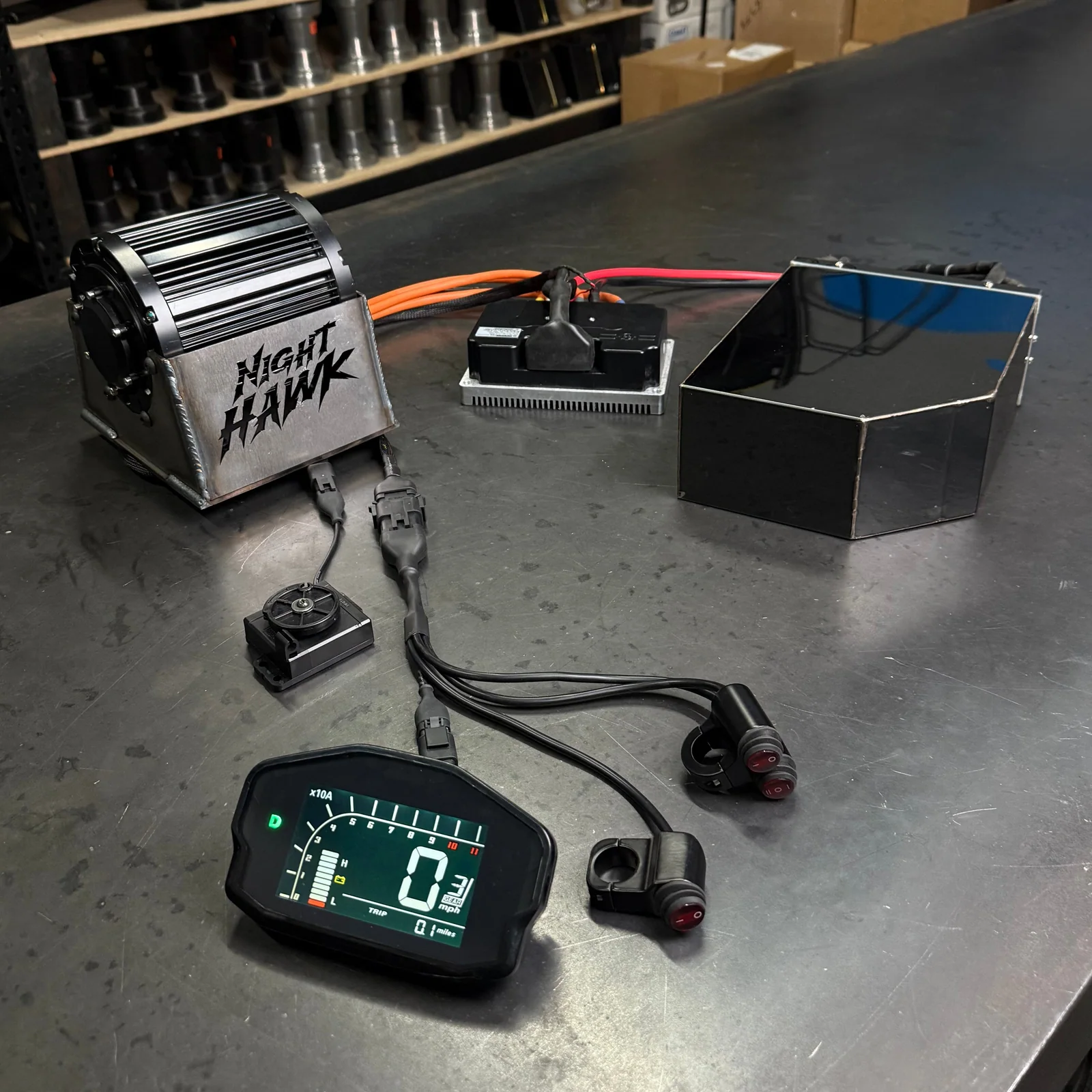 Motor eléctrico Nighthawk, controlador, caja de batería, pantalla y cableado sobre un banco de taller